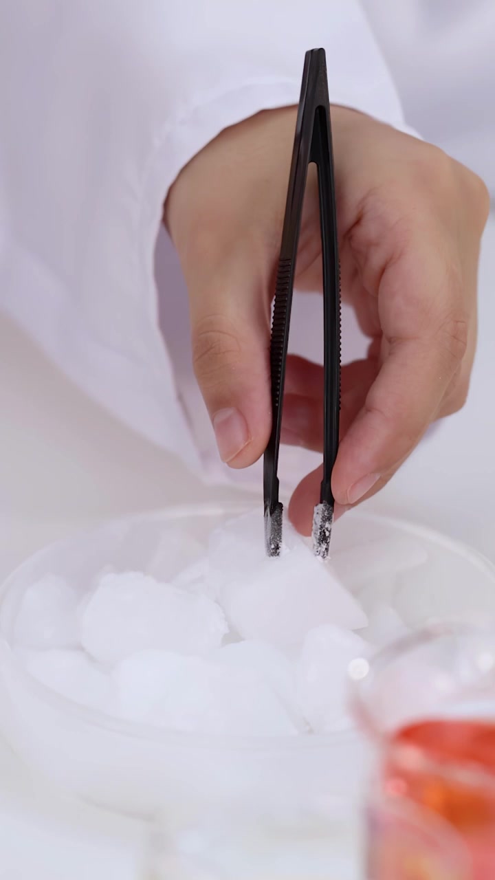 Close-up of child's hand using tweezers to pick up white solids in a petri dish.