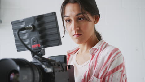 Female-Videographer-With-Video-Camera-Filming-Movie-In-White-Studio