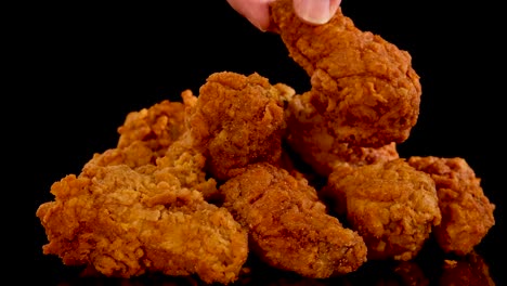 a hand slowly picks up and replaces spicy fried chicken pieces from a pile, shot in slow motion with dramatic lighting and a black background