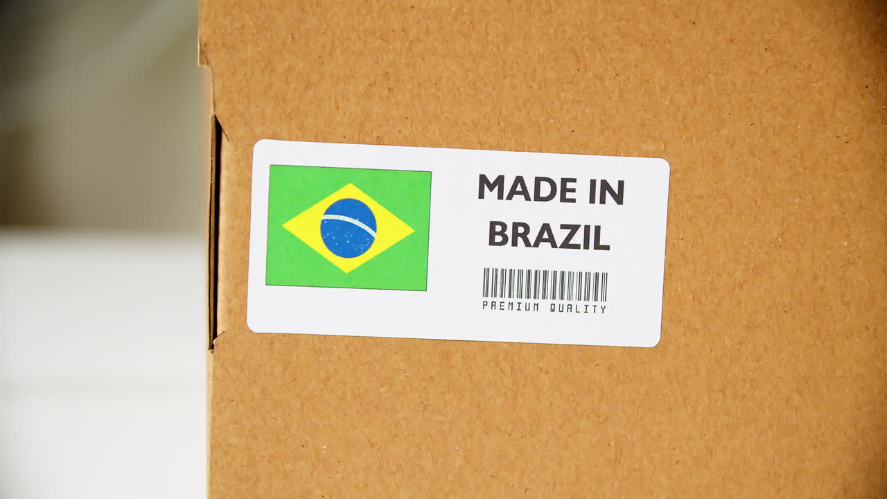 manos aplicando la etiqueta de la bandera hecha en brasil en una caja de cartón de envío con productos