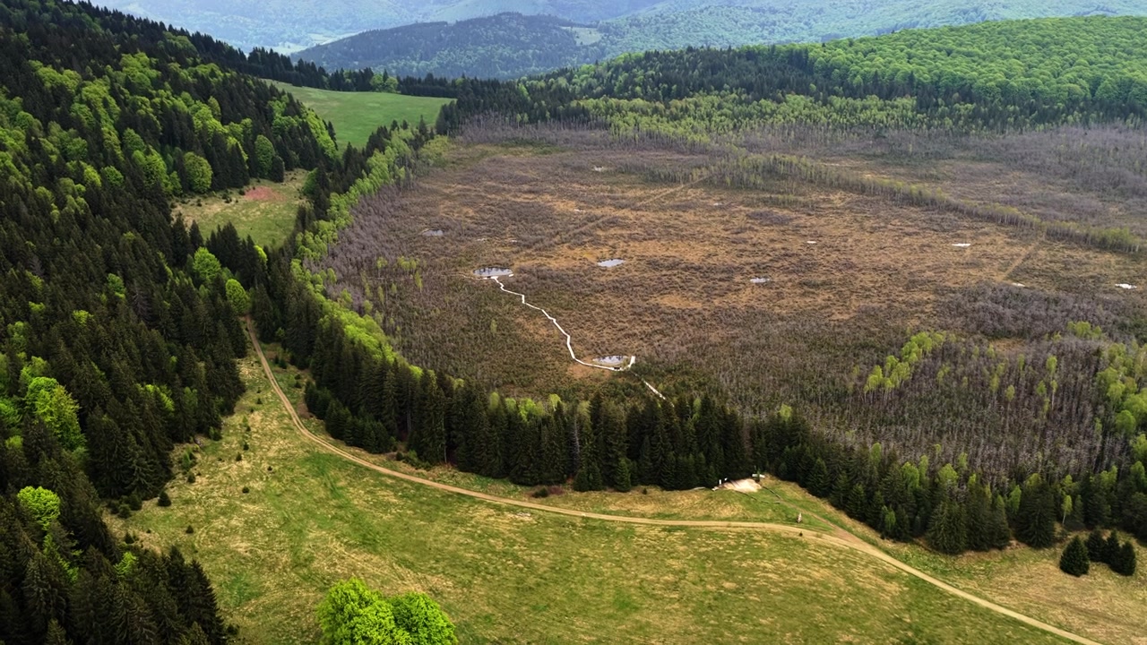 Dronebillede fra luften af en rund kratersø i en skovklædt lavning med en fjern dal, Lacul Sfanta Ana, Harghita, Rumænien