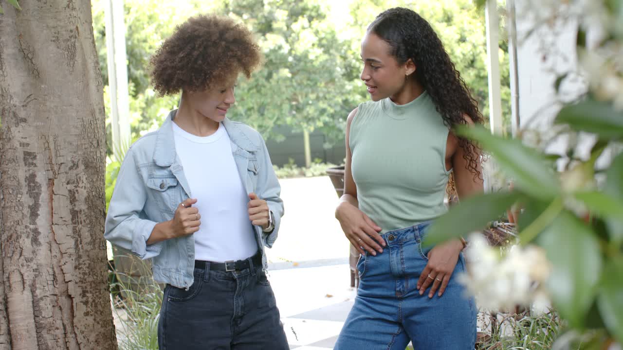 Mulheres afro-americanas conversando, apontando para uma jaqueta jeans e blusa verde no caminho, preparando-se para posar.