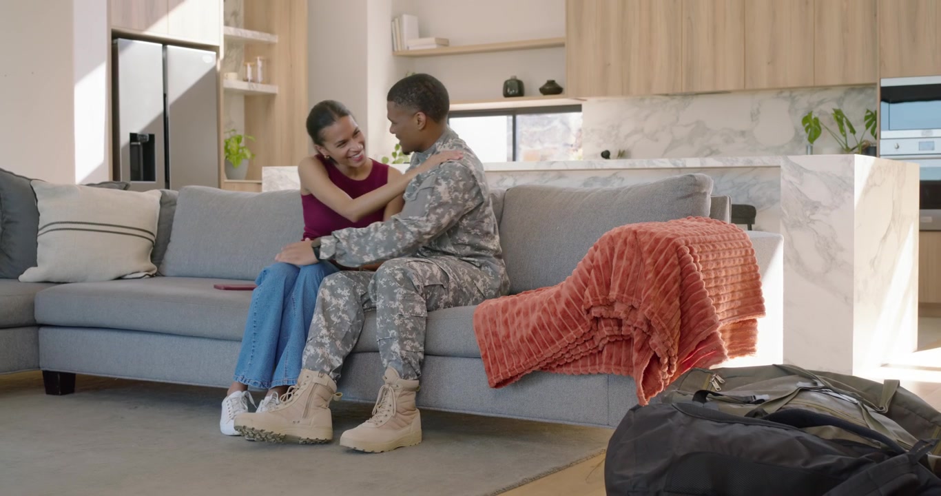 African American couple reuniting after tour uniformed man hugging examining palms on couch duffel