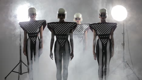 four women in futuristic costumes posing in a studio setting