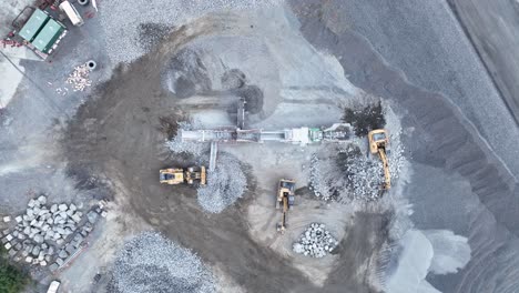 Drone-stationary-shot-of-bob-cat-and-mining-excavator-moving-rocks,-with-conveyor-belt-sorting-rocks-with-rubble-into-piles-in-quarry-mine