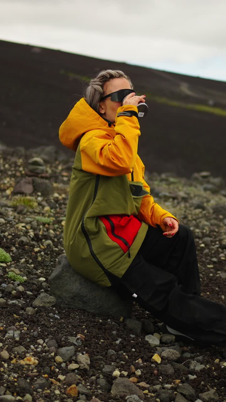Woman in Yellow Jacket Drinking from Cup on Rocky Terrain