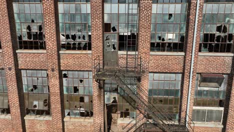 close up view of old brick industrial building facade with shattered windows and a rustic metal fire escape, conveying urban decay and historical architecture