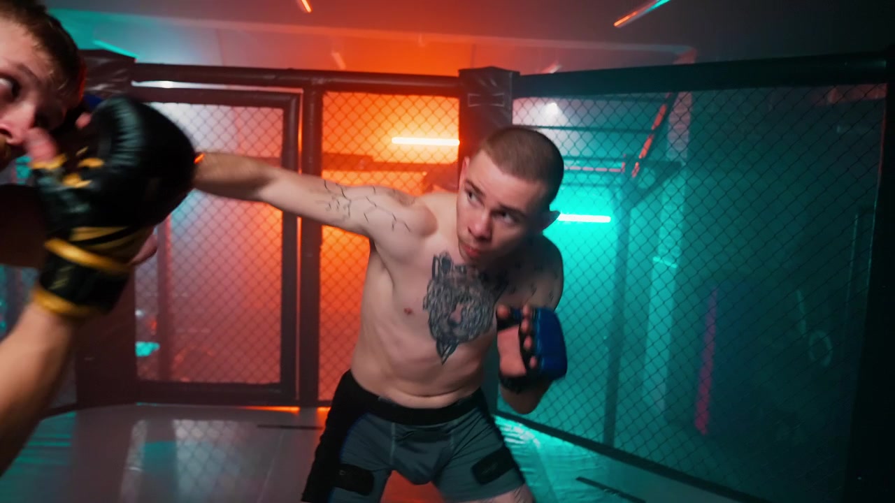 To mandlige kæmpere sparrer i et MMA-bur med neonlys
