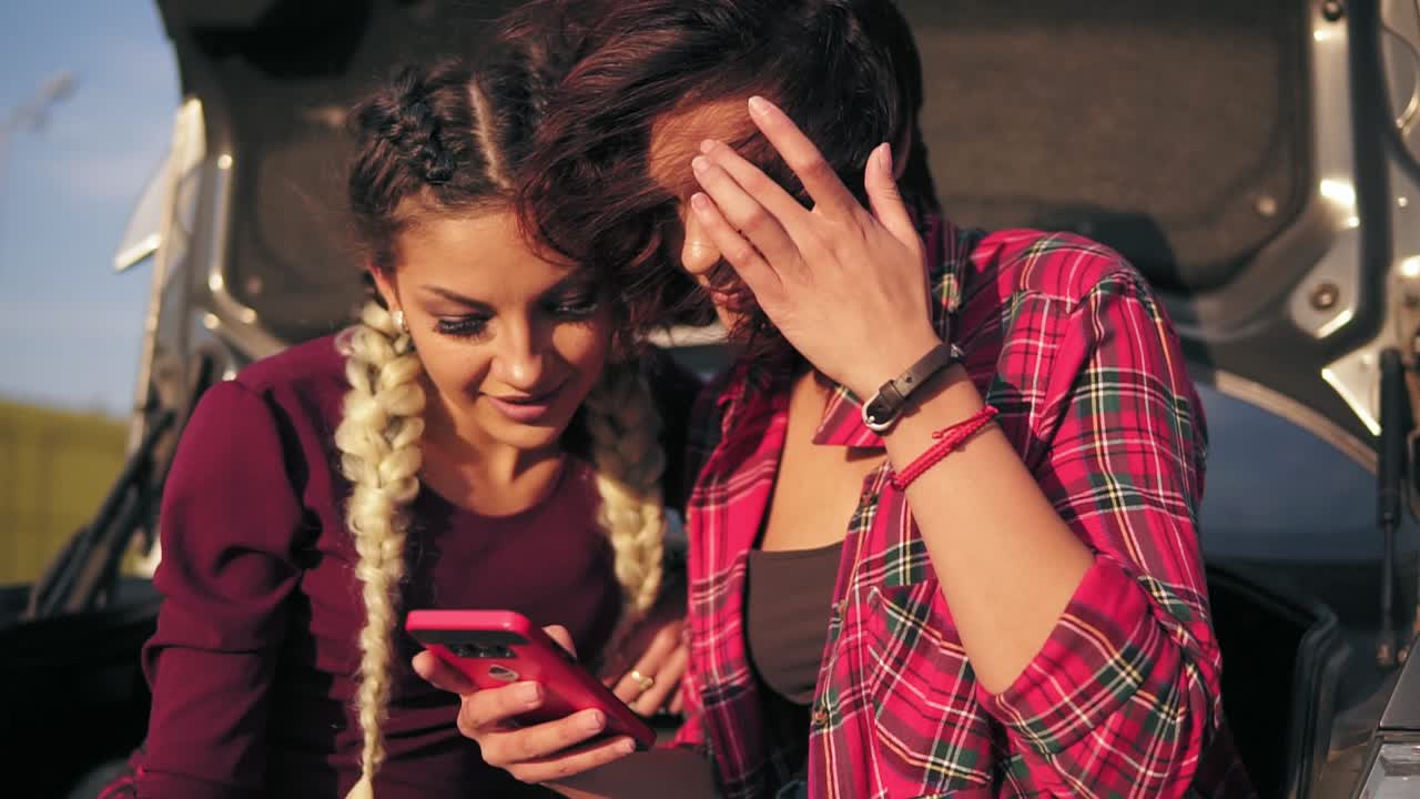 vista de cerca de dos jóvenes amigas atractivas sentadas dentro del maletero del coche abierto en el estacionamiento junto al centro comercial y