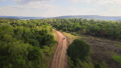 Grey-SUV-drives-fast-along-dirt-road-as-dust-flies-into-air,-drone-ascends-from-behind