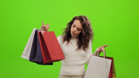 la mujer está recogiendo las bolsas de compras y examinándolas. está levantando la cabeza y mirando a la cámara. está de pie sobre un fondo verde. pantalla verde. 4k.