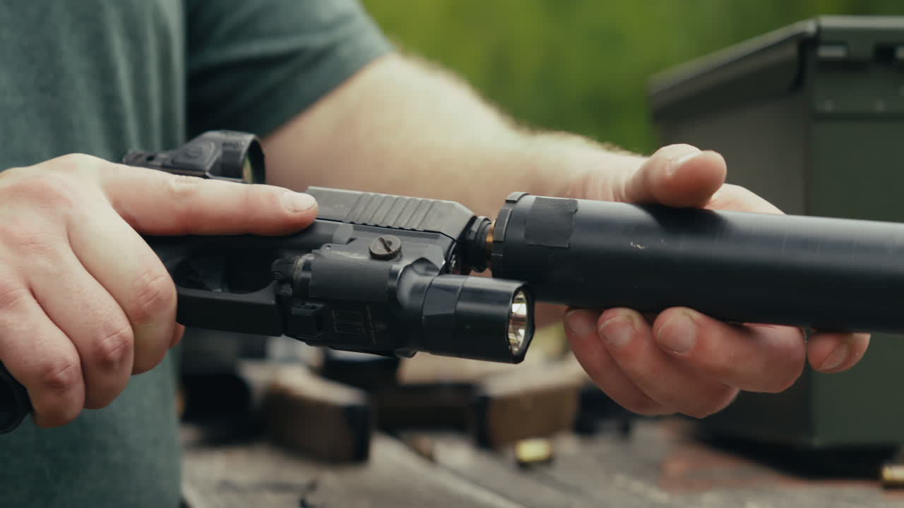 Close-up of a pistol with suppressor and red dot sight being handled