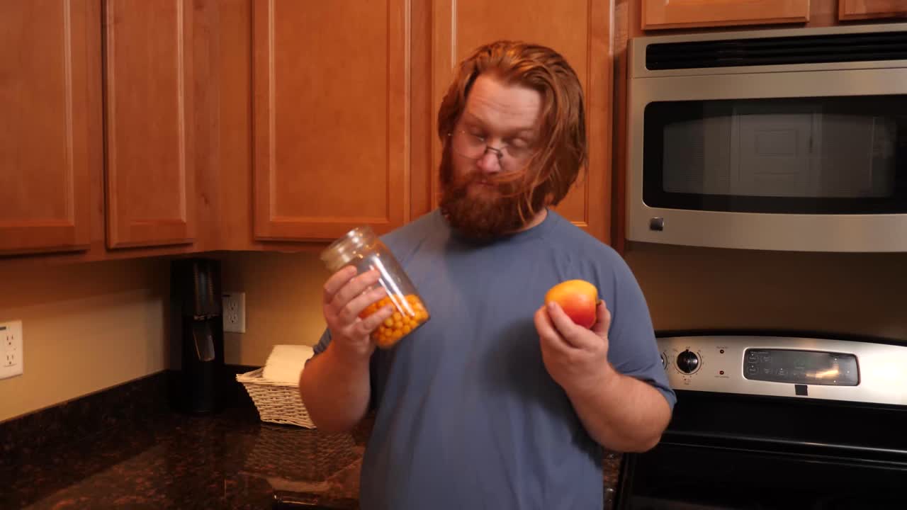 un hombre pelirrojo comparando las papas fritas con una manzana en una cocina casera.