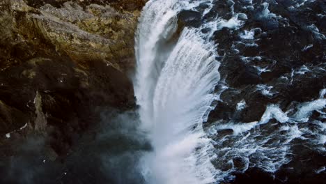 the drone captures cinematic aerial shots revealing a perilous view below, where a rapid waterfall plunges from rugged stone cliffs