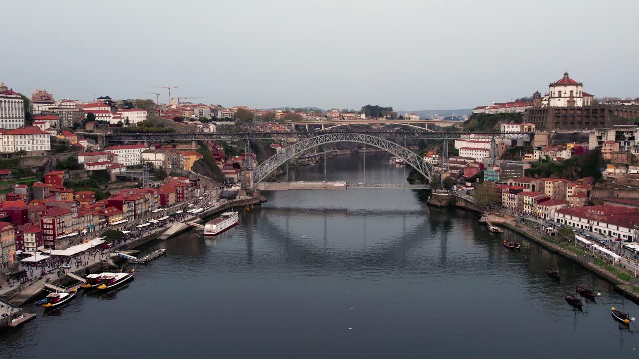 Douro River flowing through Porto, Portugal, showcasing the iconic Dom Luis I bridge connecting the historic Ribeira district and Vila Nova de Gaia with traditional buildings lining the riverfront