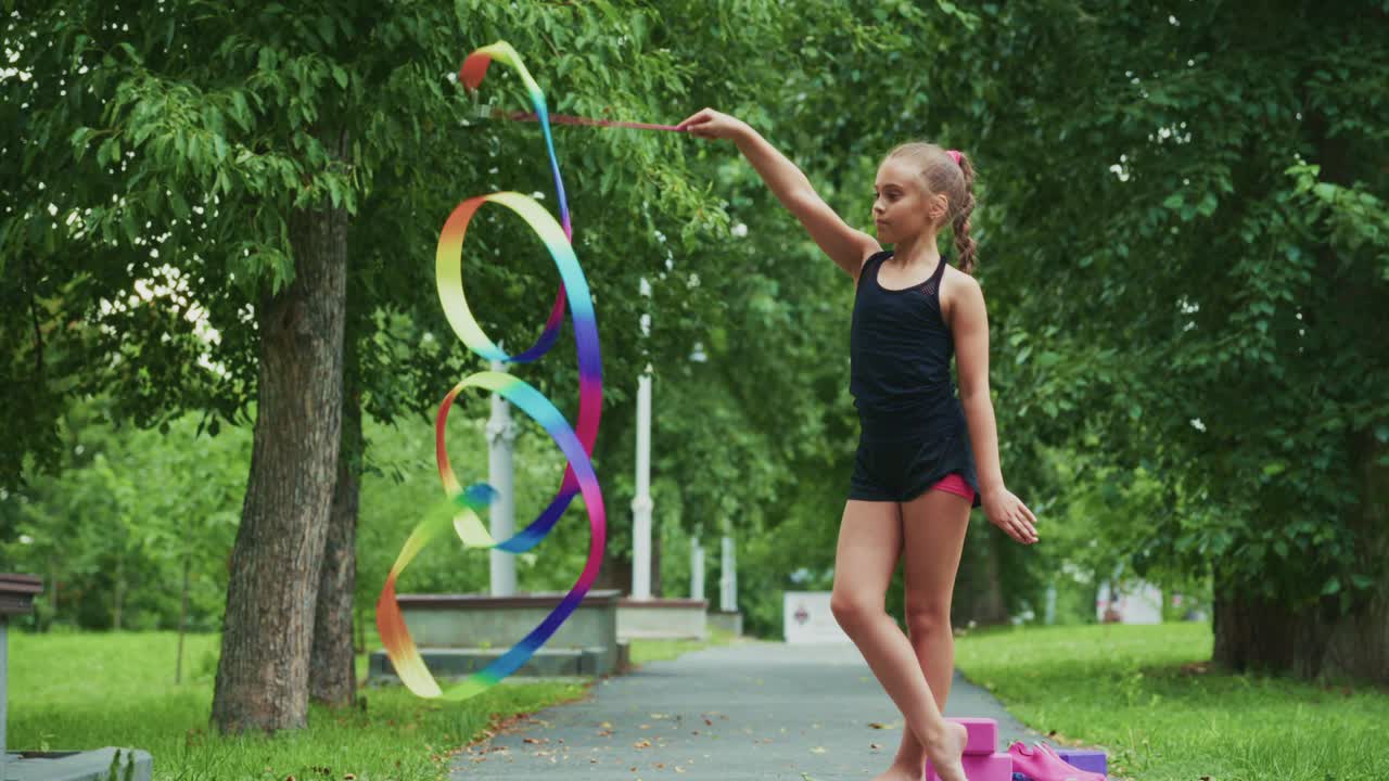 A Young Girl Displays Her Grace and Skill with Colorful Ribbons in a Lush Park, Showcasing Rhythm and Movement in a Captivating Dance Performance