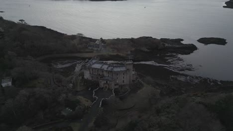 Castillo-De-Dunvegan-En-La-Isla-De-Skye,-Rodeado-De-árboles-Y-Agua-Al-Atardecer,-Vista-Aérea