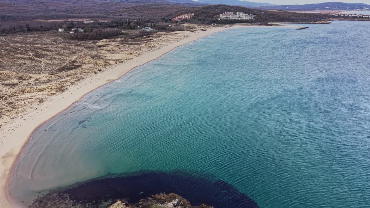 Coastal view of a sandy beach surrounded by gentle waves and hills