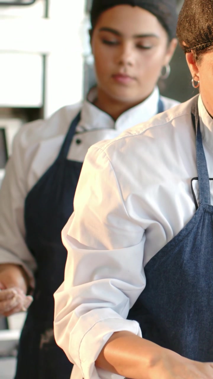 Video vertical: Chef inclinado con bata blanca y delantal vaquero, estirando masa para hornear, espacio para texto.
