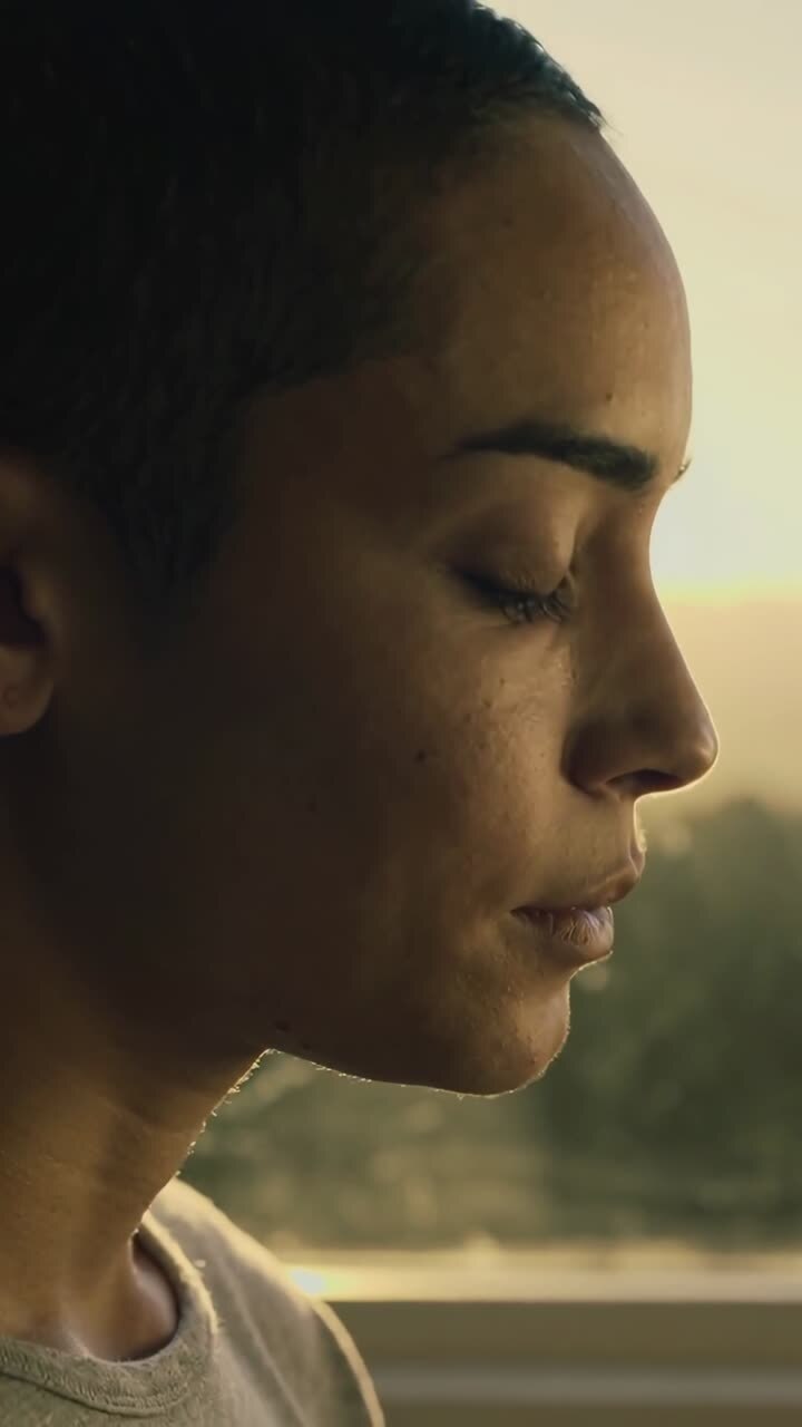 Vertical video: Reacting to golden-hour light, woman pressing lips opening eyes at window, crew tee