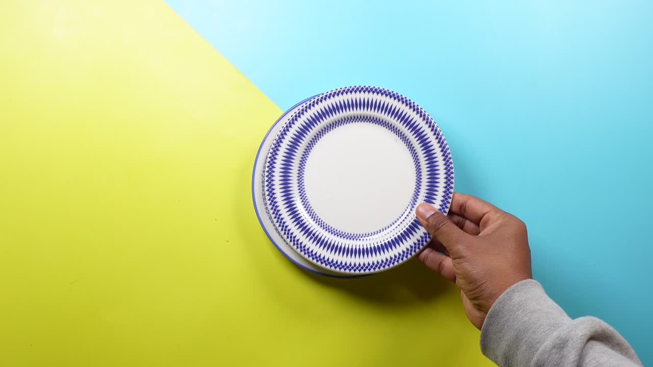 una mano sosteniendo una placa blanca con un patrón azul contra un fondo amarillo y azul