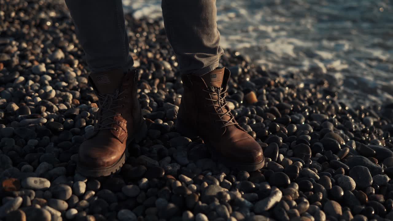 persona con botas en una playa rocosa al atardecer