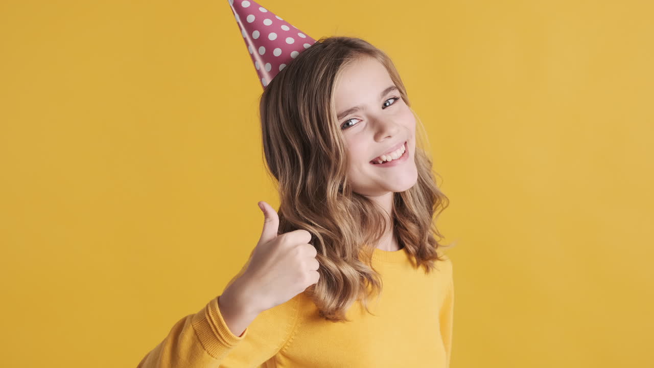 una adolescente caucásica con los pulgares hacia arriba con un sombrero de fiesta.