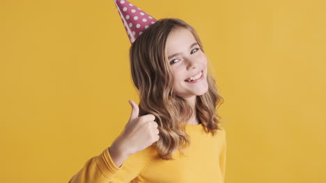 teenage caucasian girl with thumbs up wearing a party hat.