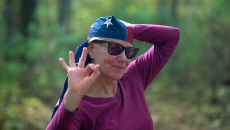 closeup of pretty, blonde woman wrapping an american flag around her head and giving the camera the peace or victory sign and laughing