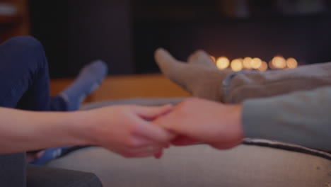 close up of romantic couple relaxing holding hands and warming feet by fire at home