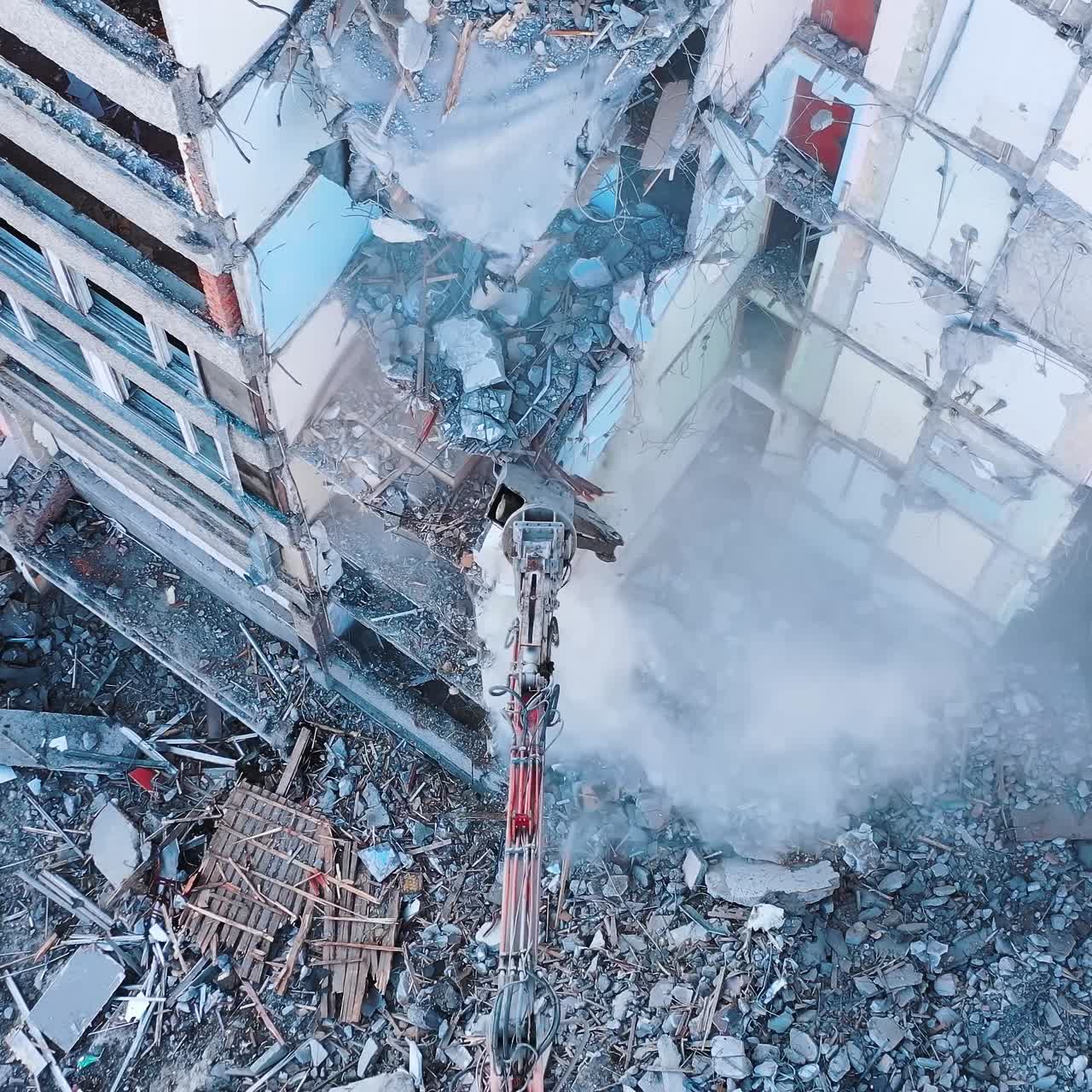 Demolishing machinery breaks the floors and walls of the ruin. Debris falling down with heavy dusty clouds. Rising over the ruins and debris