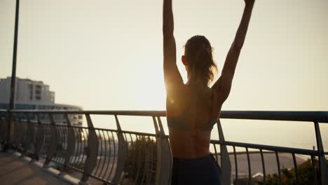 a young girl in a sports summer uniform stretches against the backdrop of a sunrise