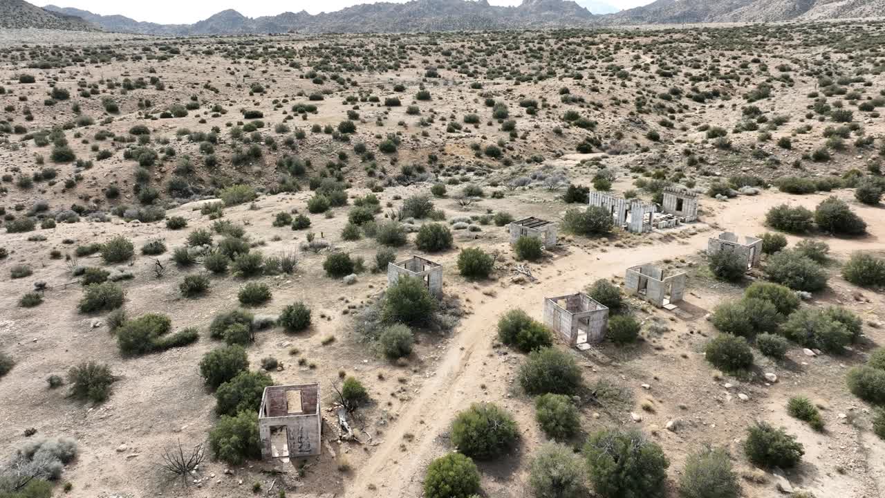 Strutture in cemento di un edificio abbandonato distrutte dal cartello nell'alto deserto della California meridionale in una giornata nuvolosa con un'atmosfera apocalittica. ORBITA AEREA 60fps