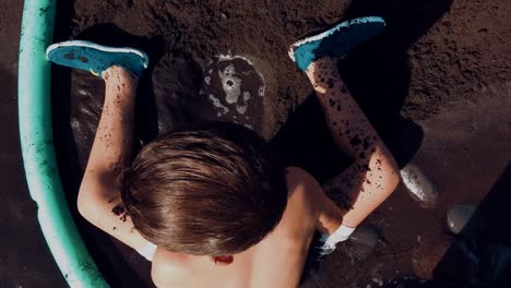 seaside boy playing with dark beach sand while a wave breaks arround him