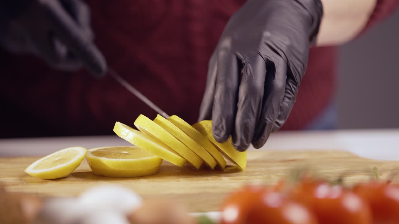 Close-up of hands in black gloves slicing a ripe lemon on a wooden board. The fresh citrus fruit is perfect for cooking, drinks, and garnishing meals, adding a zesty and refreshing touch to any dish