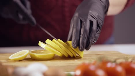 close-up of hands in black gloves slicing a ripe lemon on a wooden board. the fresh citrus fruit is perfect for cooking, drinks, and garnishing meals, adding a zesty and refreshing touch to any dish