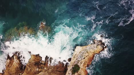 Gorgeous-top-down-aerial-drone-footage-of-a-scenic-rocky-cliff-with-wild-waves-crashing-and-creating-foam,-Chalkidiki,-Greece
