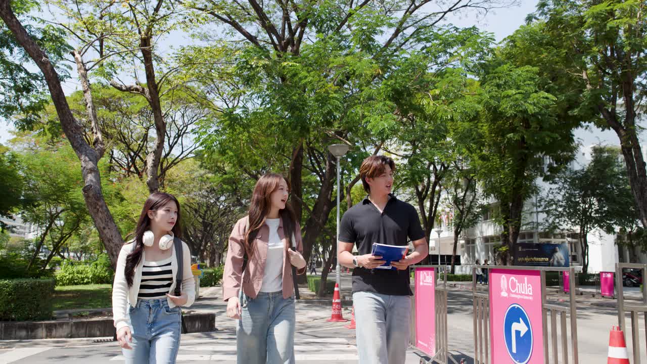 햇살 좋은 대학교 캠퍼스를 이야기하며 학습 자료를 들고 걷는 아시아 학생들.