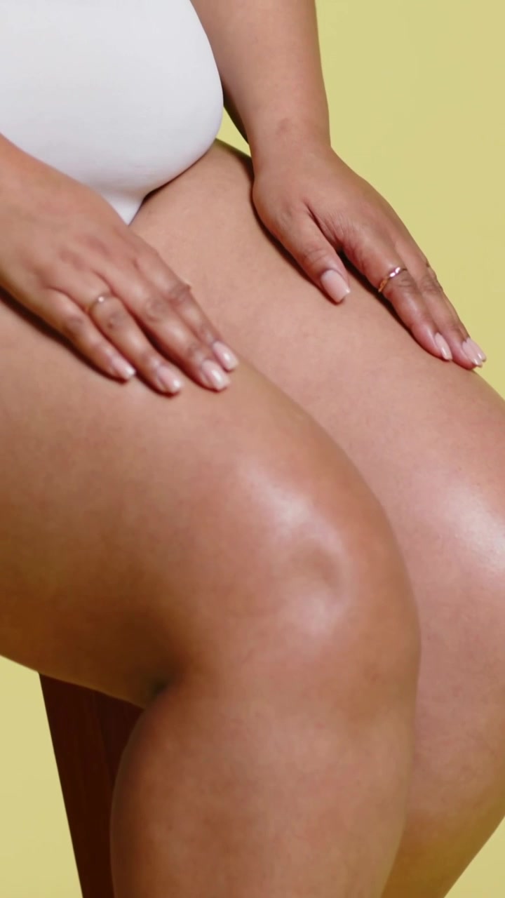 Video verticale: Telecamera che si allontana da una modella che si liscia le cosce su uno sgabello in studio, indossa slip bianchi e anelli d'oro.