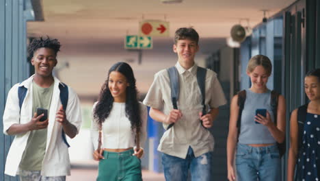 multi-cultural high school or secondary students walking outside classrooms looking at phones