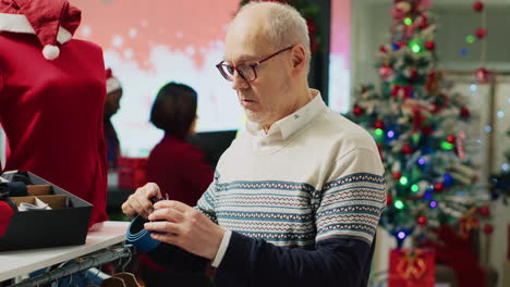 cliente anciano mirando cinturones, admirando la hermosa artesanía mientras compra en la tienda decorada con navidad. viejo cliente en la boutique de moda del centro comercial en busca de regalos de navidad para ofrecer a la familia