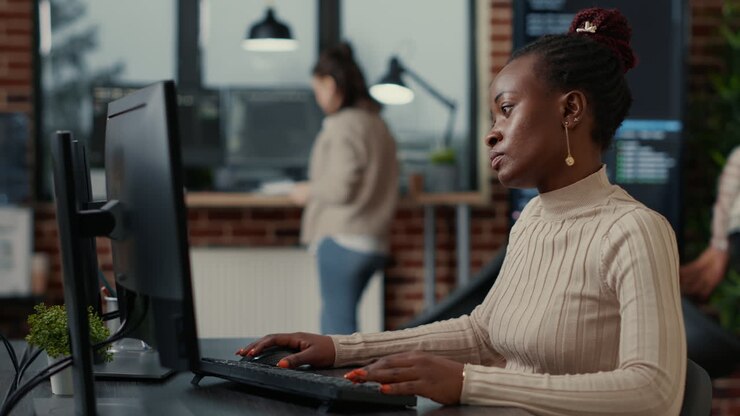 Afroamerikanische SoftwareentwicklerIn arbeitet konzentriert und schaut auf den Computerbildschirm, während sie tippt
