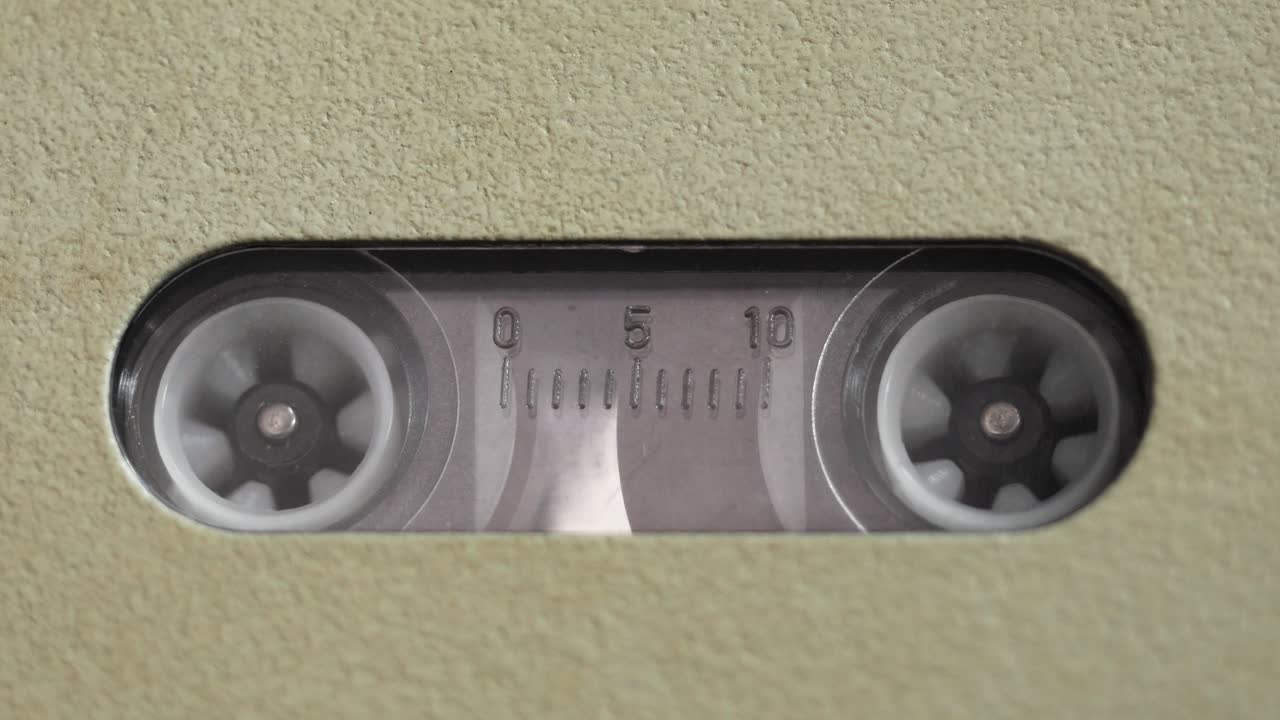 Carretes de cinta girando dentro de la ventana de una grabadora de voz vintage beige, toma macro cenital directa