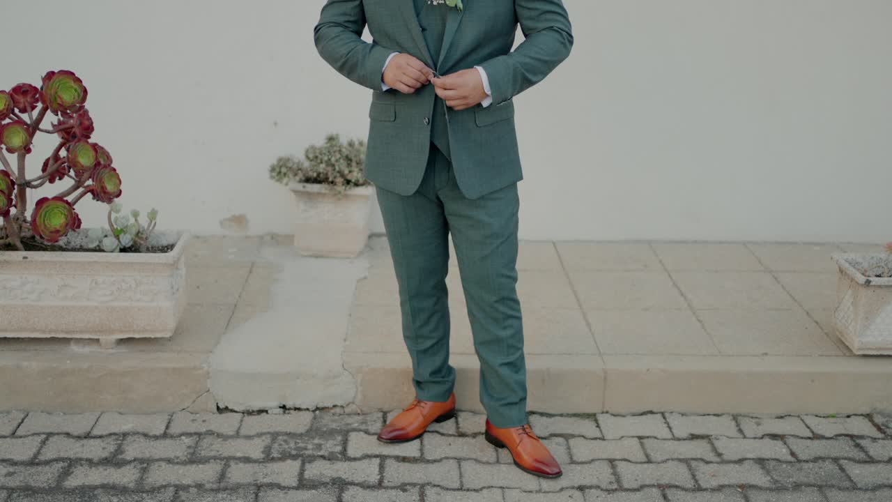 비 식물 근처의 야외 산책로에서 초록색 슈트와 갈색 신발을 조정하는 남자