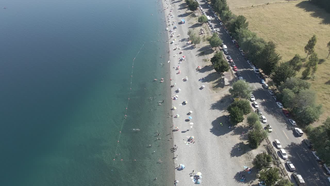 vista aérea del lago ranco en chile con gente en él, un camino pavimentado con árboles y aguas azules profundas