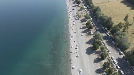 Aerial-view-of-the-Ranco-lake-in-chile-with-people-on-it,-a-paved-road-with-trees-and-the-deep-blue-waters