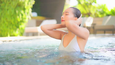 Sexy-exotic-woman-touching-her-wet-hair-in-a-swimming-pool-on-tropical-vacation,-full-frame-slow-motion