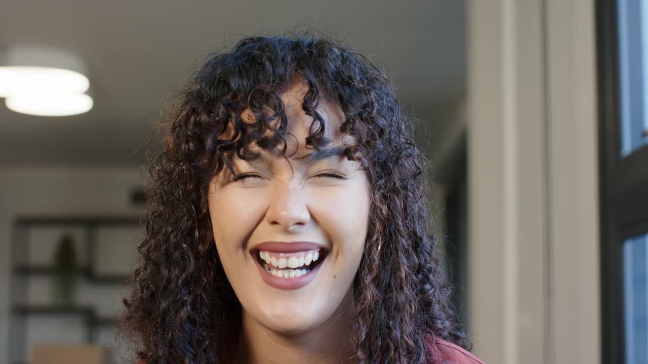 African American woman reacting to joke, smiling, laughing at home in red top with pendant lamp