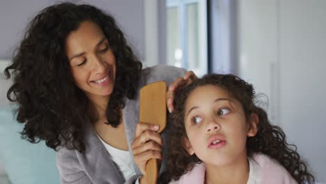 madre e hija de raza mixta feliz cepillando el cabello en el dormitorio