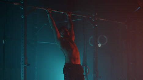 athletic man is training hard in gym in night hanging on bar and lifting legs up